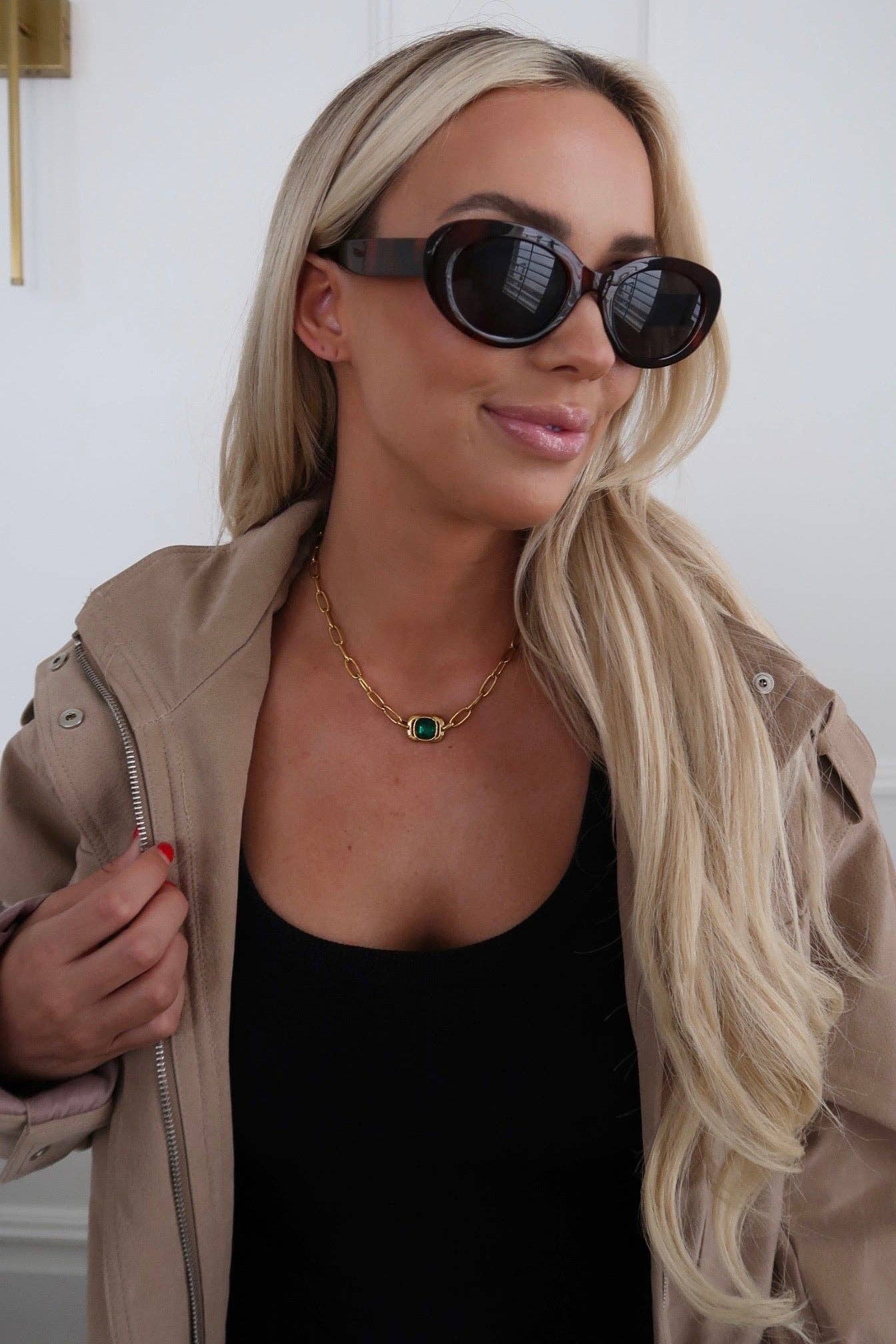 Woman wearing sunglasses and a beige jacket indoors