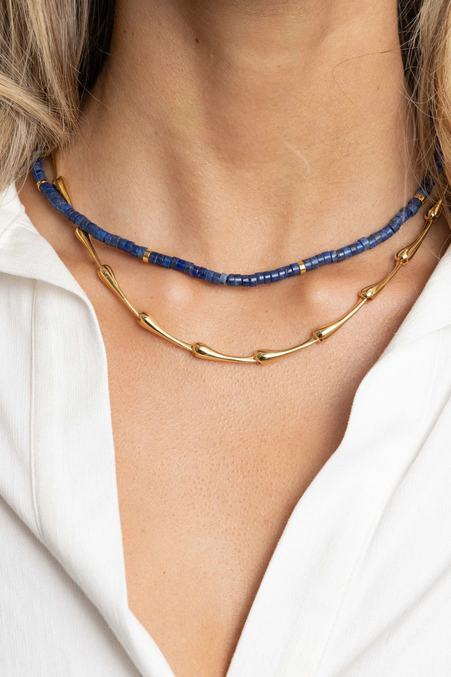Close-up of a person wearing a gold and blue beaded necklace against a white background