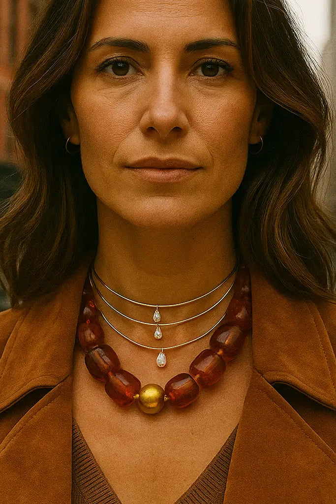 Woman wearing a brown coat and a necklace with amber beads and a gold pendant, standing in an urban setting.