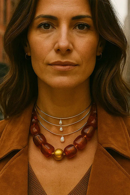 Woman wearing a brown coat and a necklace with amber beads and a gold pendant, standing in an urban setting.