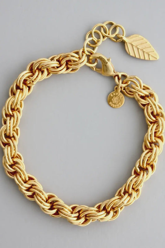 Gold chain bracelet with leaf and round pendants on a gray background