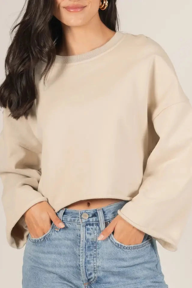 Person wearing a beige sweater and blue jeans against a plain background