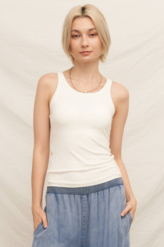 Woman wearing a white tank top and blue pants against a plain background