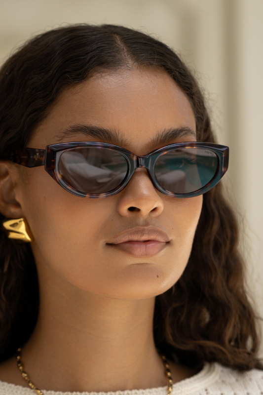 Woman wearing dark sunglasses with a neutral background