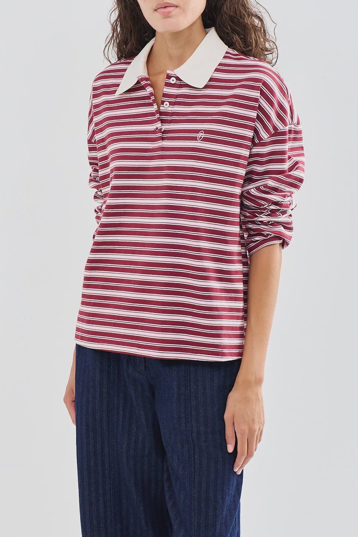 A woman wearing a long-sleeve polo shirt with horizontal red, white, and navy stripes, featuring a solid white collar and navy blue pants, against a light gray background.