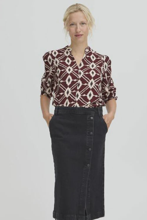 Woman wearing a patterned blouse, black skirt, and black shoes on a white background