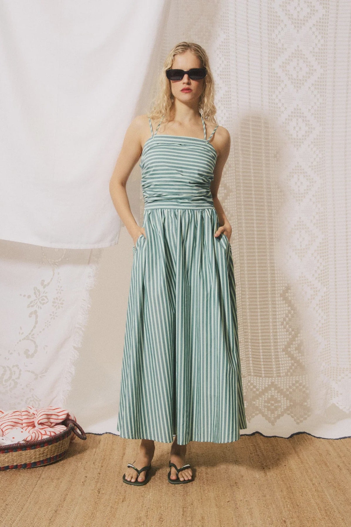 Woman wearing a green striped dress standing against a textured white wall.