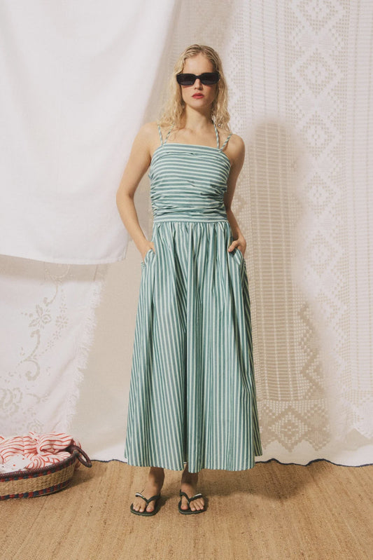 Woman wearing a green striped dress standing against a textured white wall.