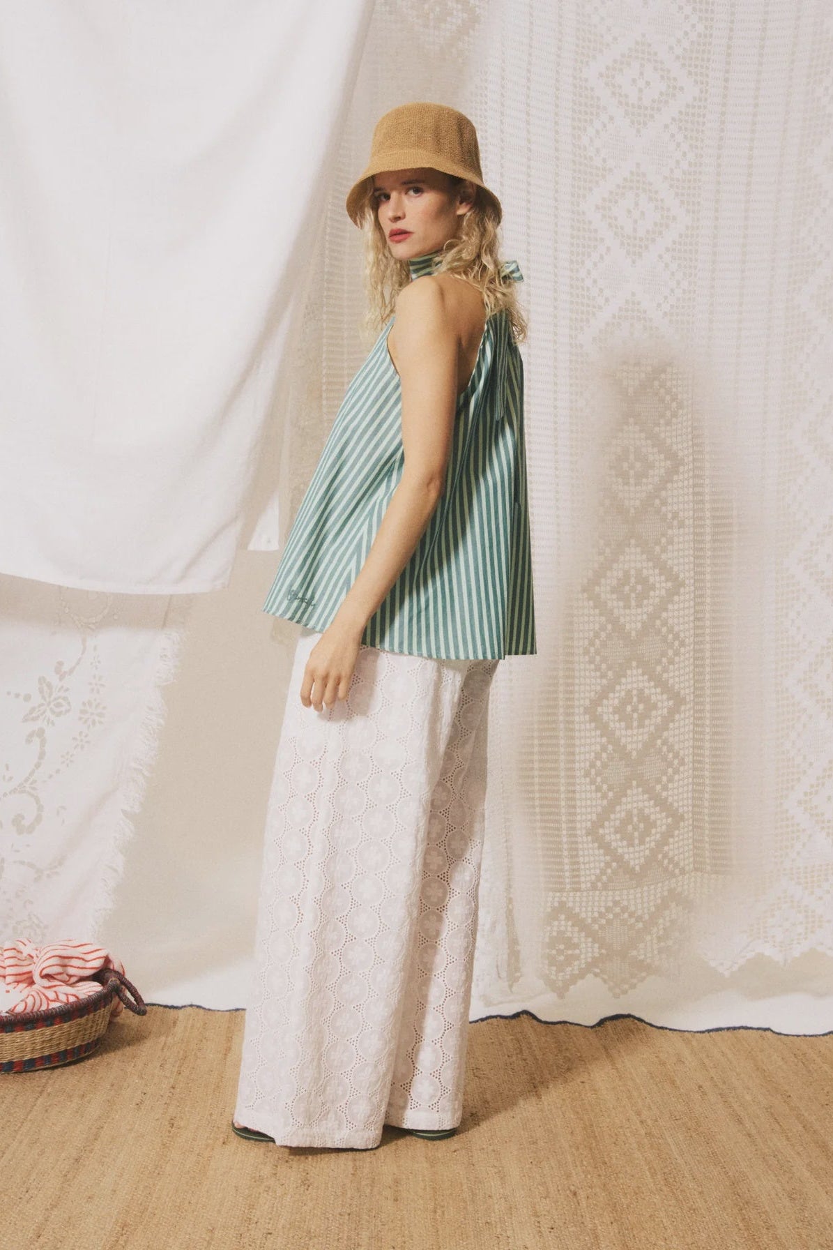 Woman wearing a striped top and wide-leg pants with a hat, standing against a textured white wall.
