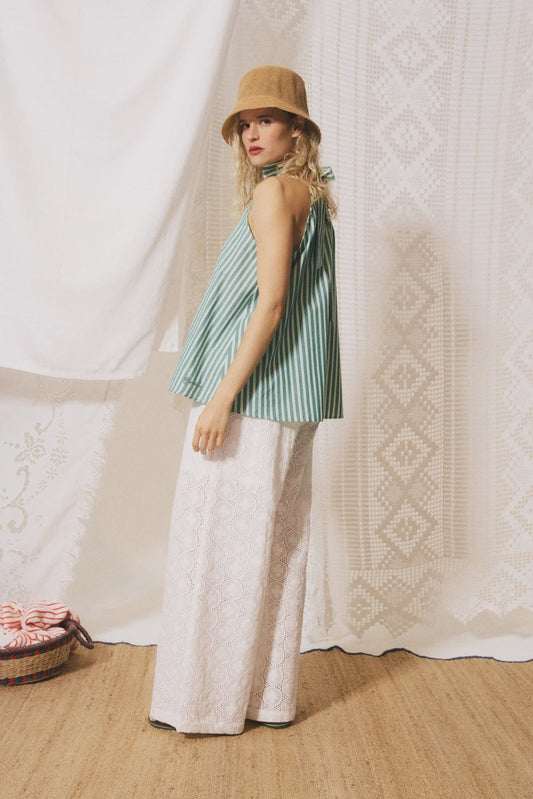 Woman wearing a striped top and wide-leg pants with a hat, standing against a textured white wall.