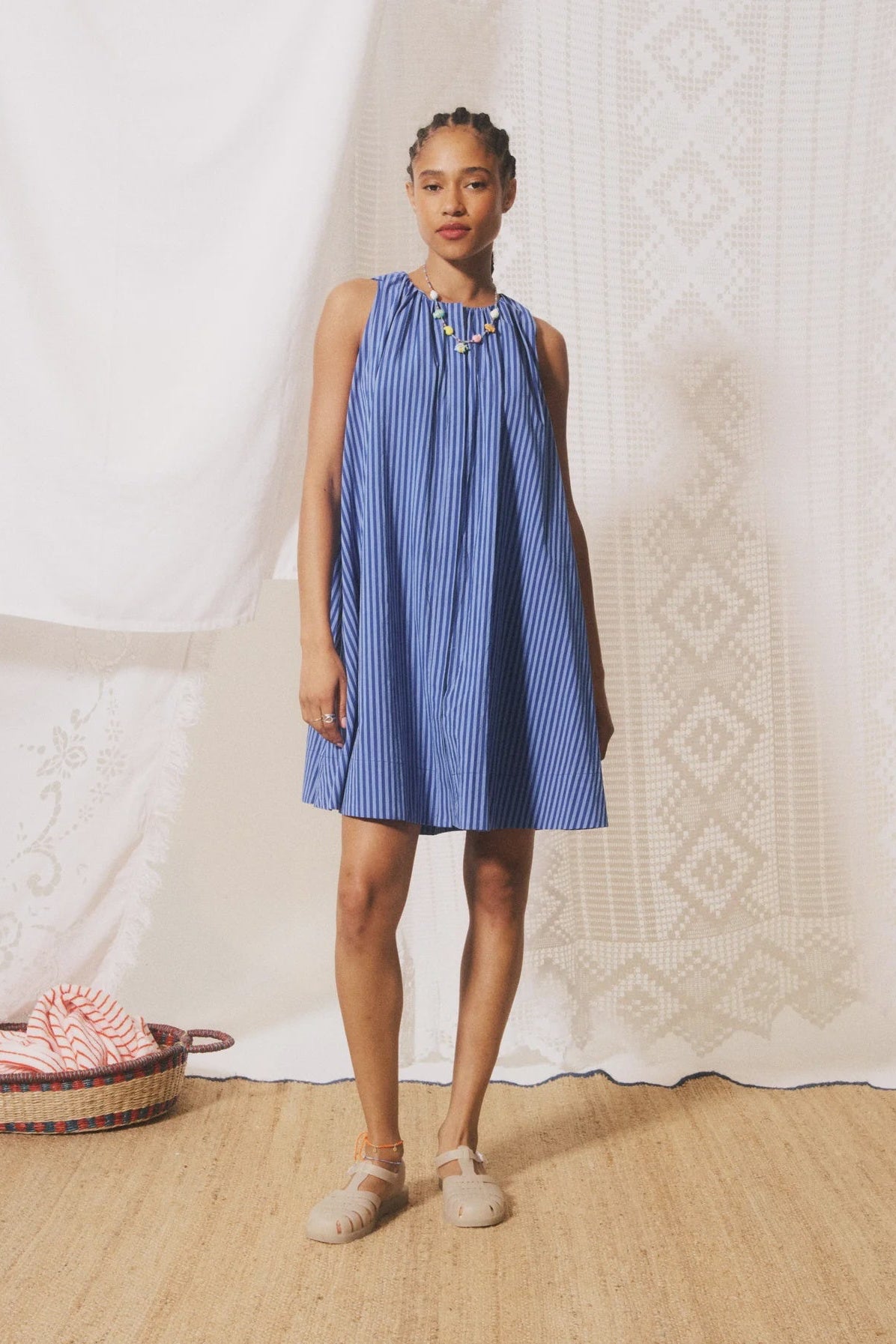 Woman wearing a blue striped dress standing in front of a white curtain.