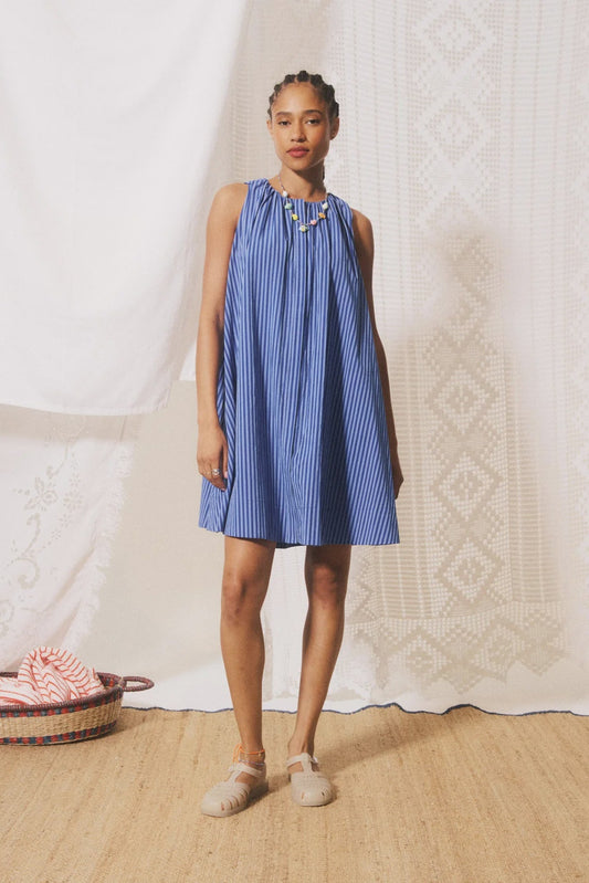 Woman wearing a blue striped dress standing in front of a white curtain.