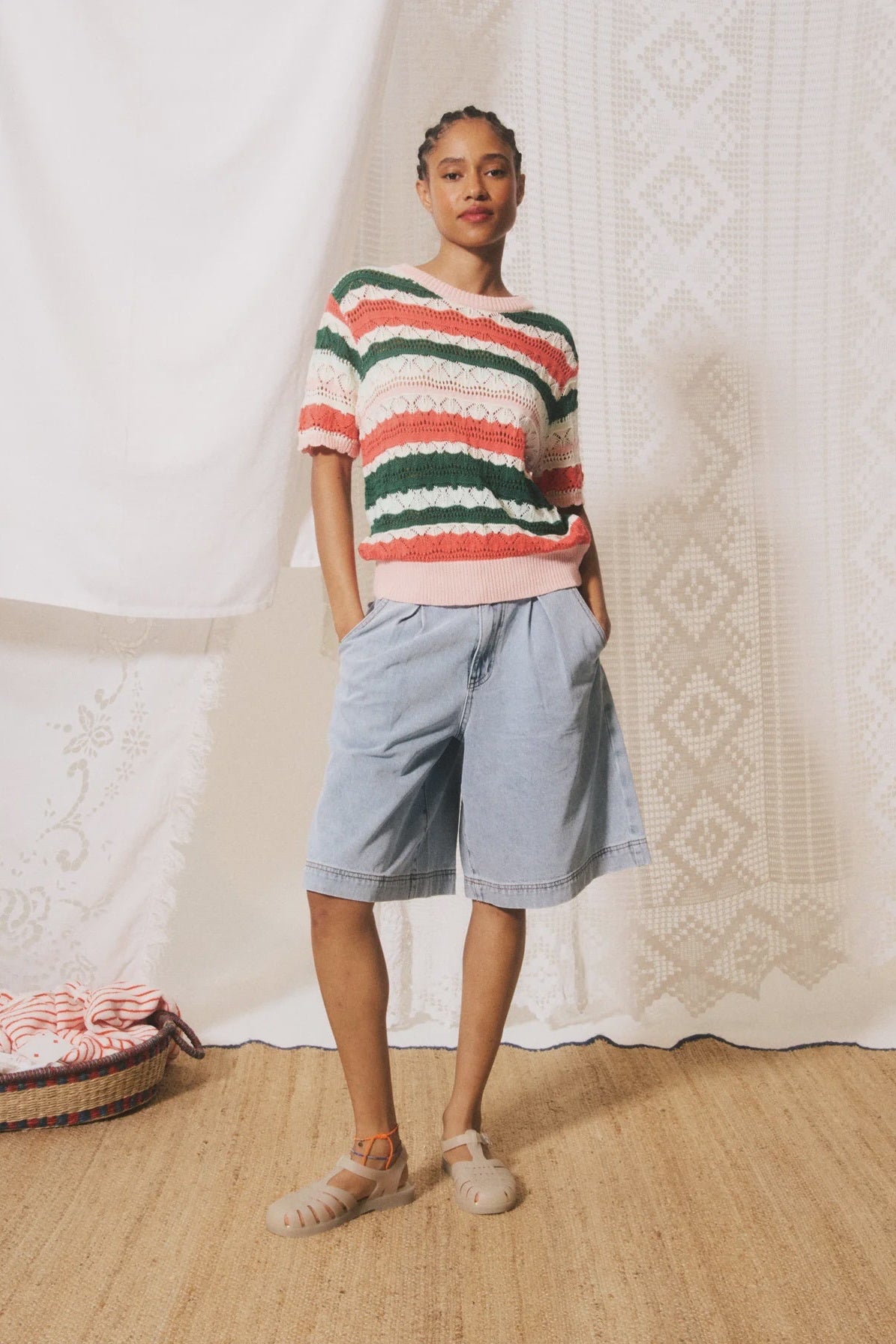 Person wearing a striped sweater and shorts standing in front of a textured white curtain.
