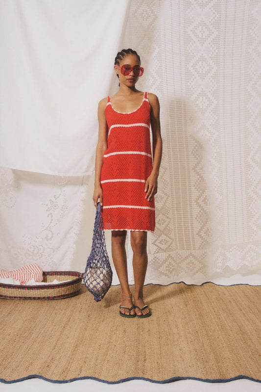 Woman in a red dress standing against a textured white wall.