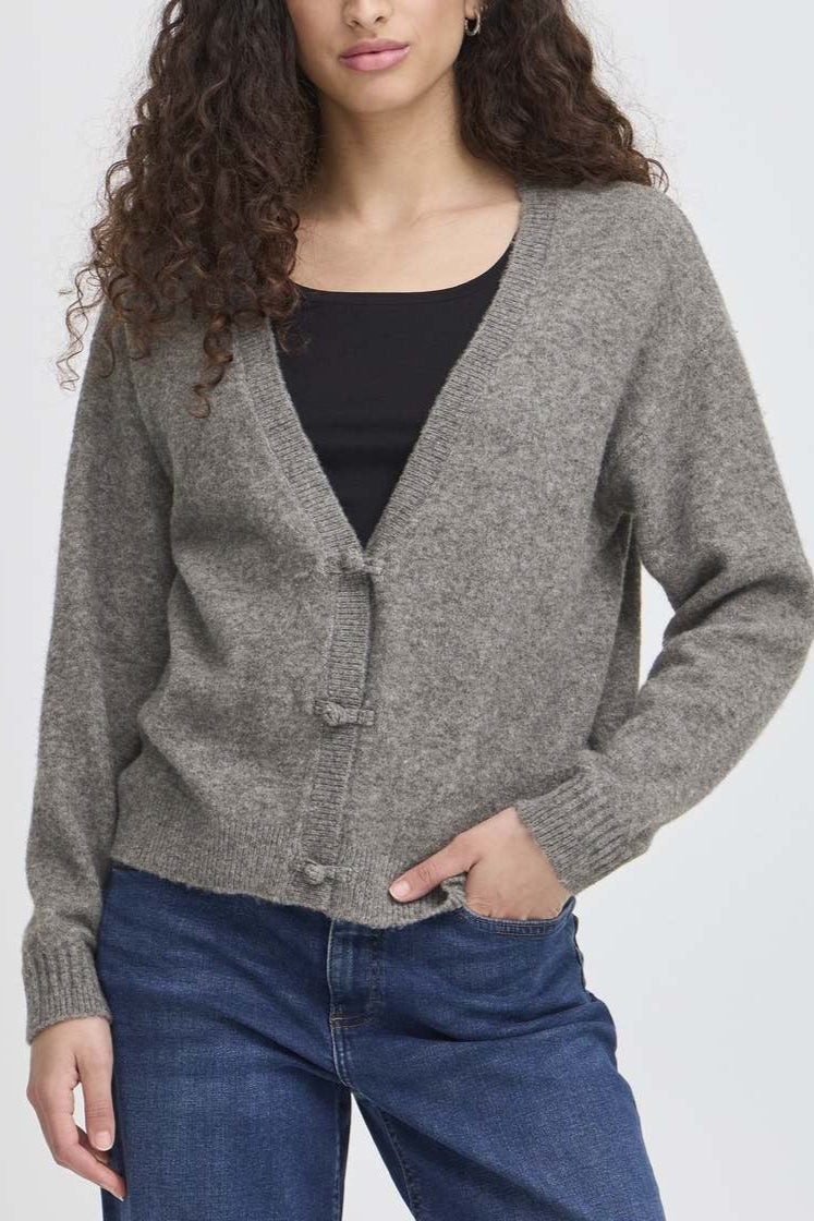 Woman wearing a gray cardigan over a black top and blue jeans on a white background