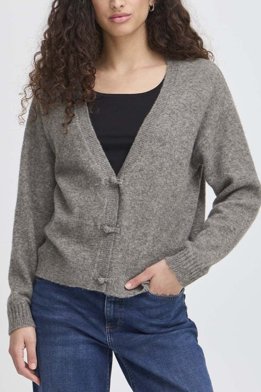 Woman wearing a gray cardigan over a black top and blue jeans on a white background
