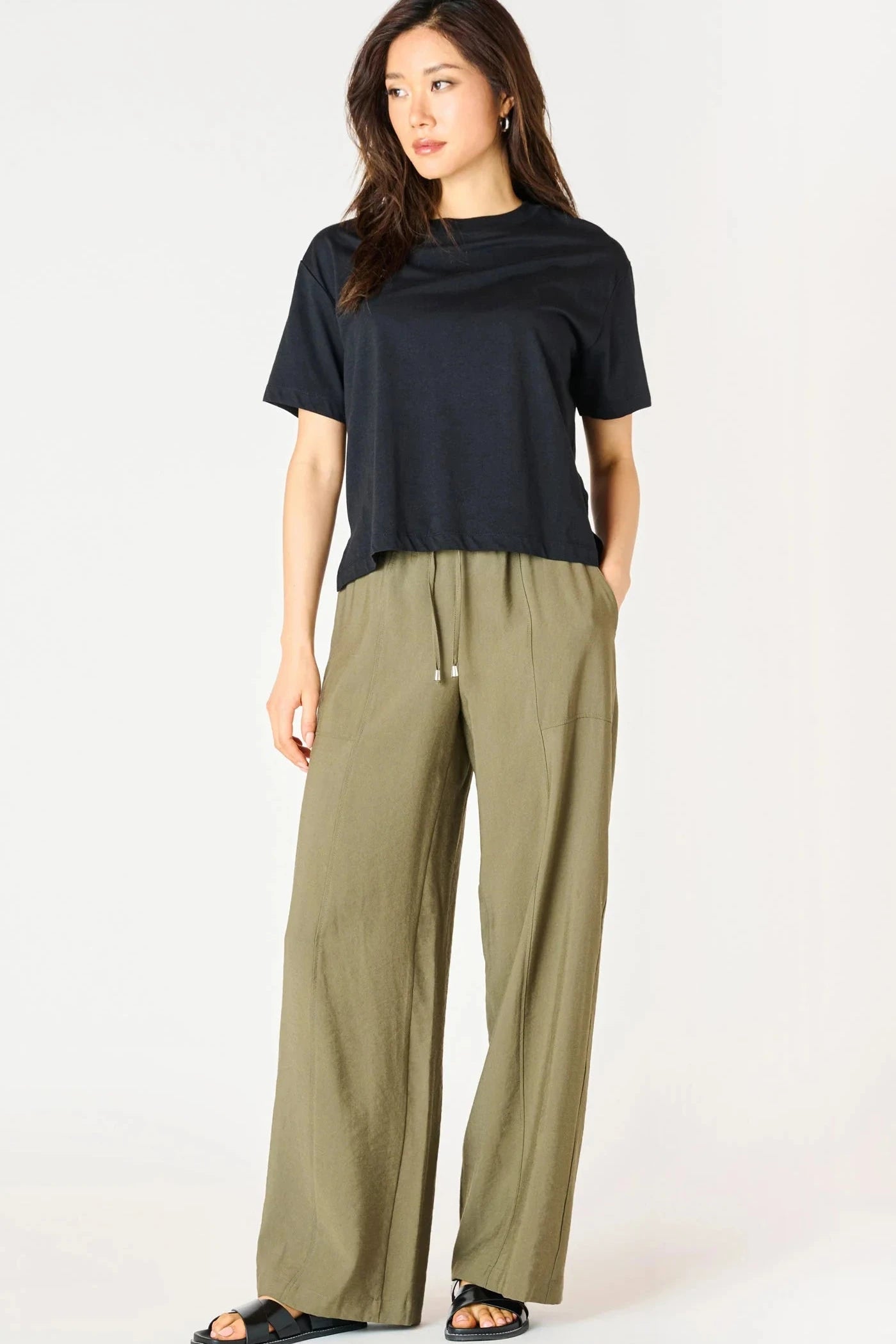 Woman wearing a black top and olive green pants on a white background