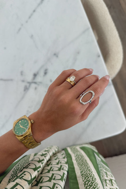 Hand wearing a gold watch and rings on a marble surface