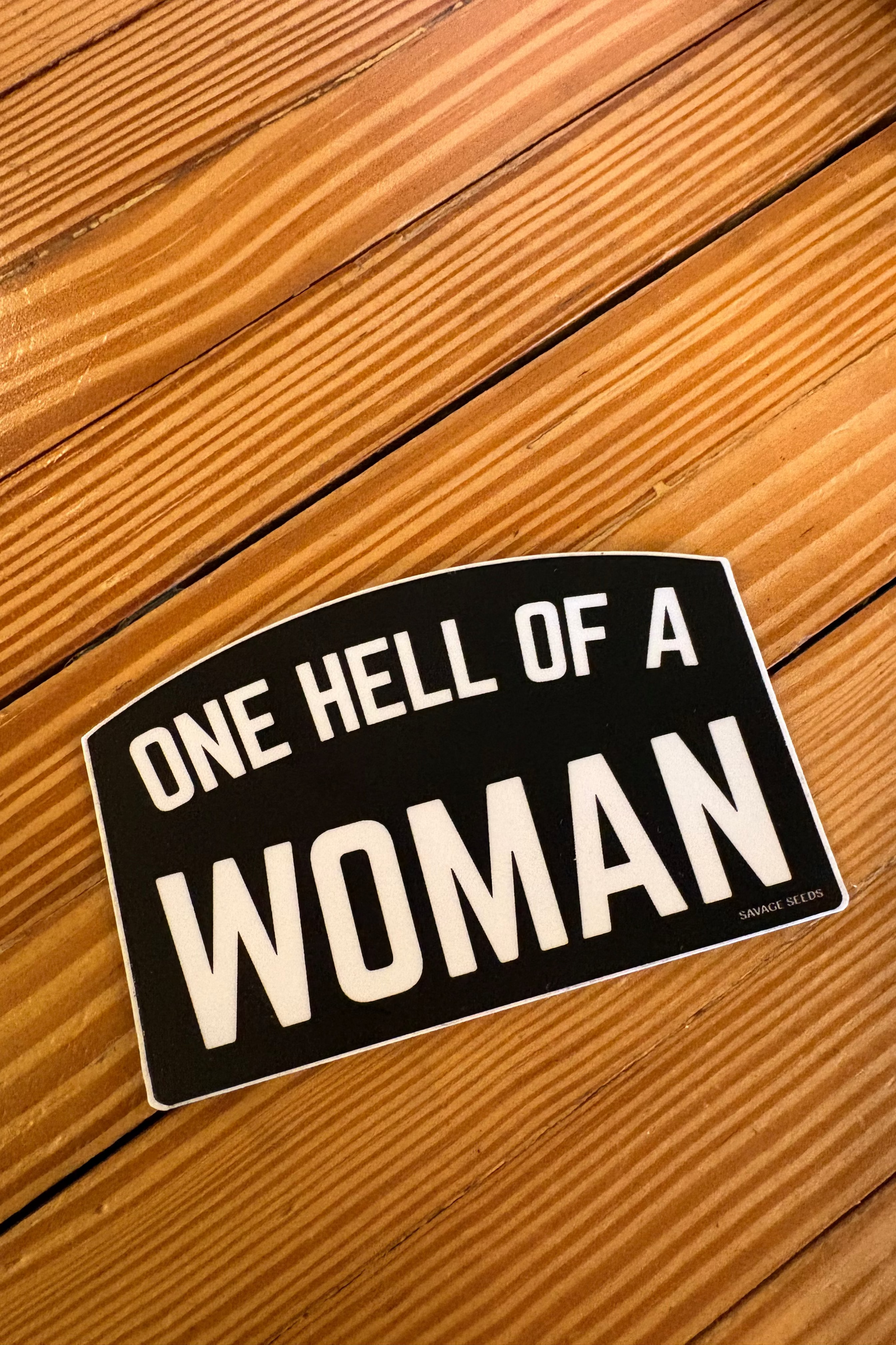 Sticker with 'One Hell of a Woman' text on a wooden surface