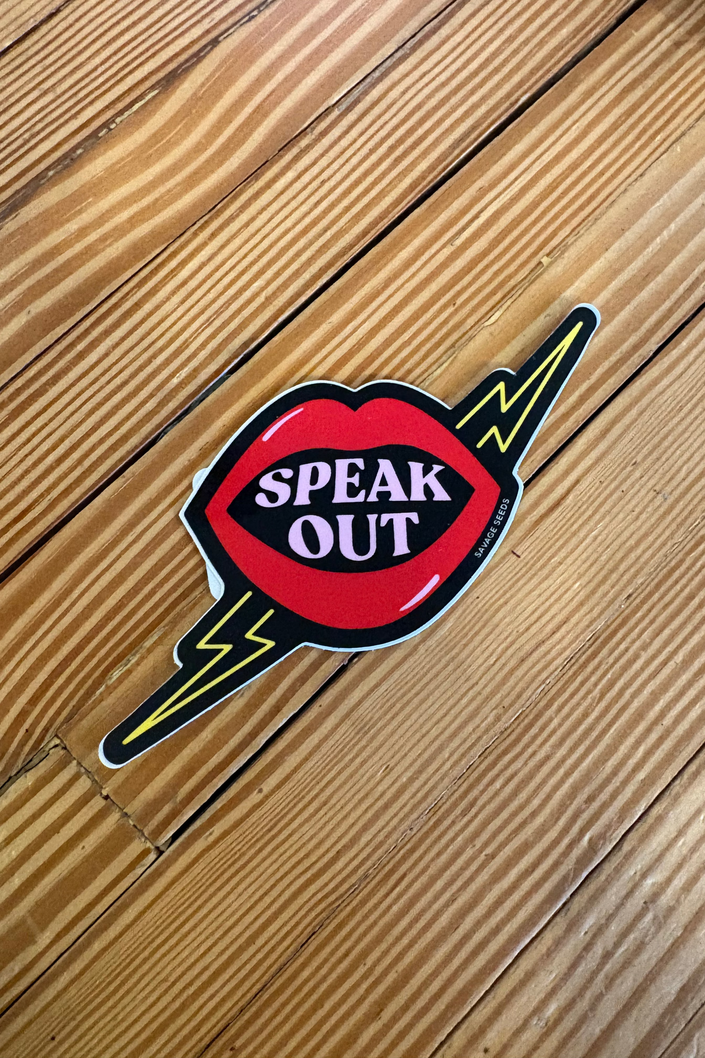 Sticker with 'Speak Out' text on a wooden surface