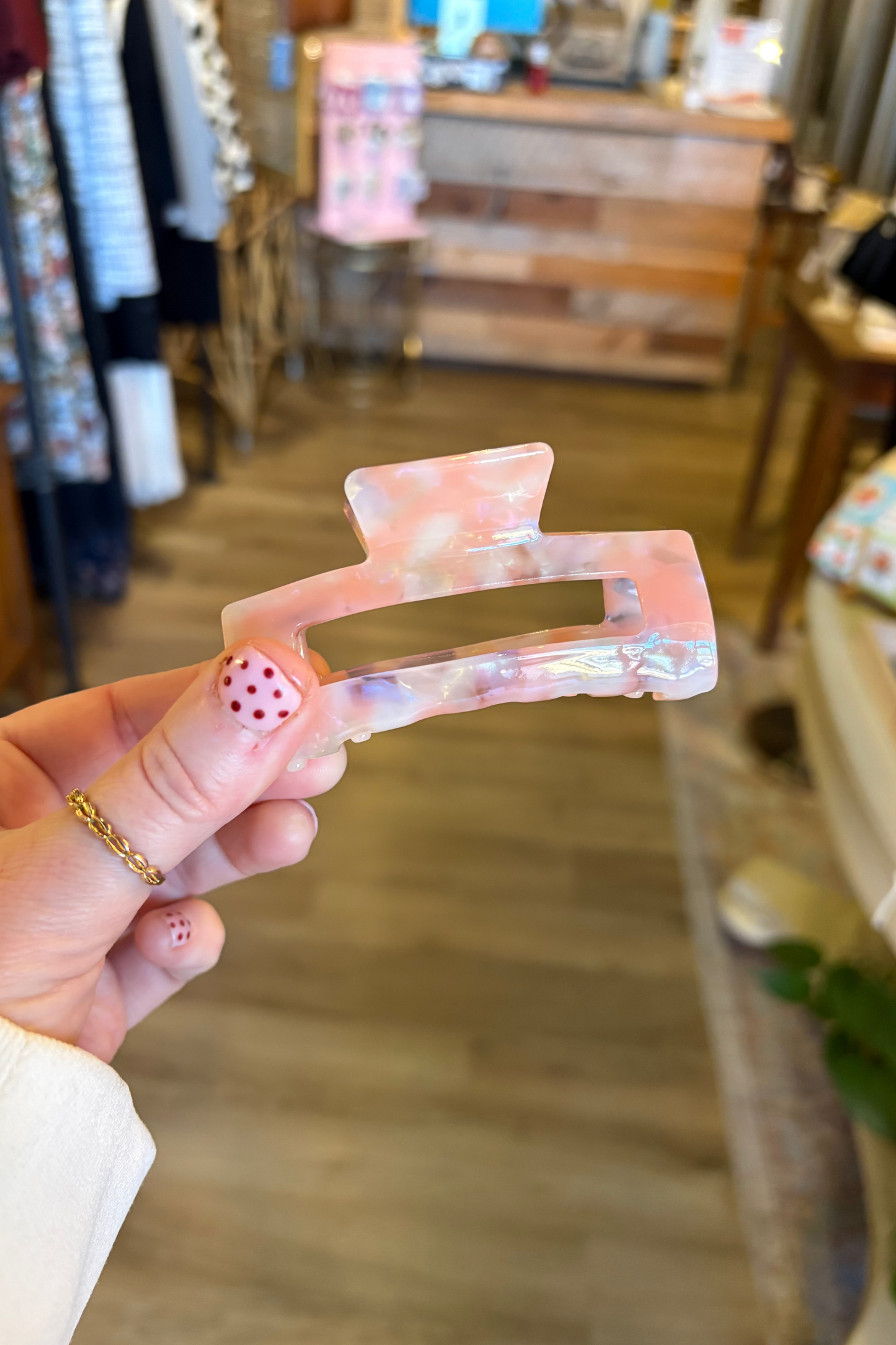 Hand holding a clear hair clip with pink and blue speckles in a store setting