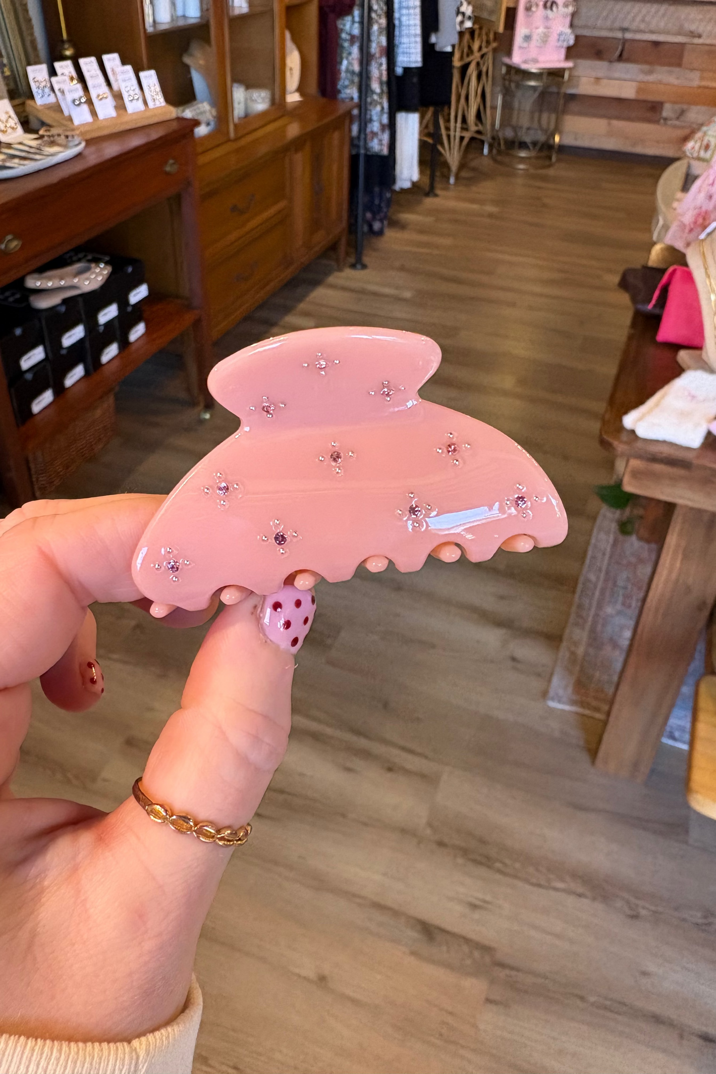 Hand holding a pink butterfly-shaped hair clip with decorative elements in a store setting.