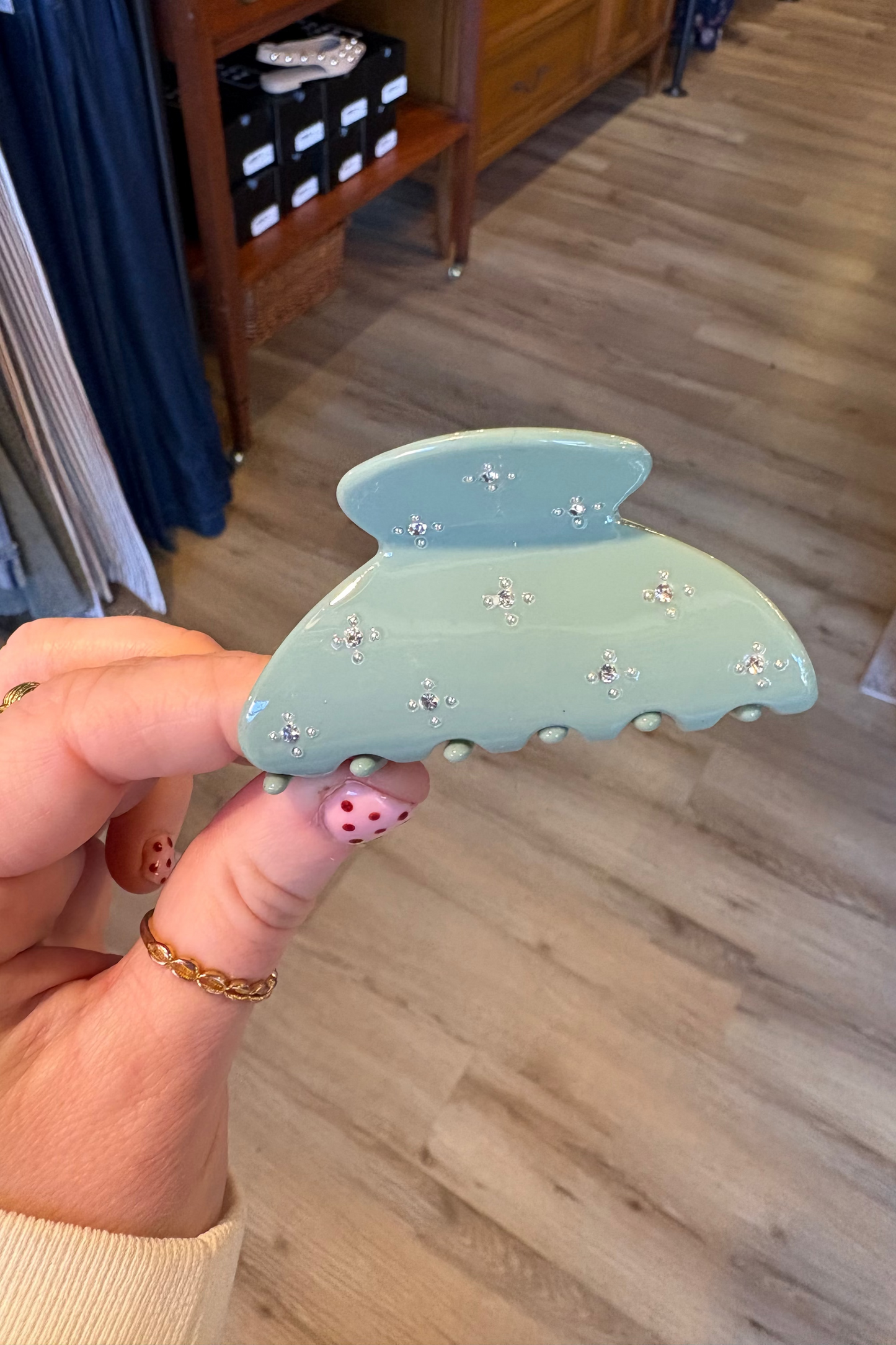 Hand holding a decorative hair clip with rhinestones in a room setting.