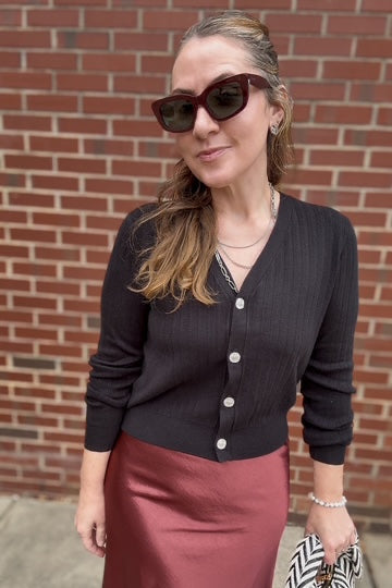 Woman wearing a black cardigan and red skirt standing against a brick wall.