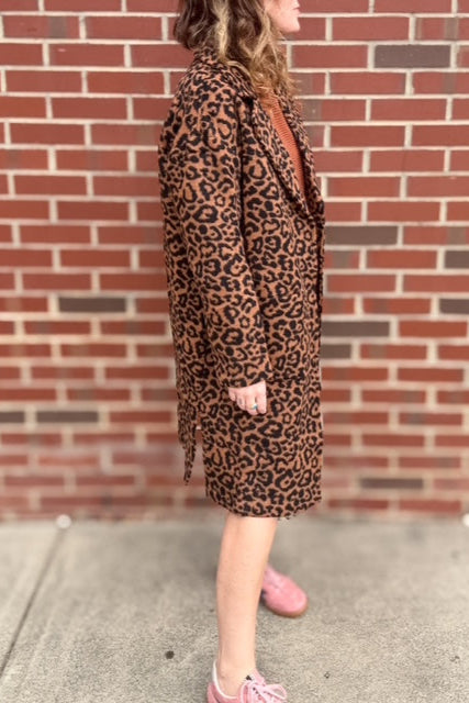 Person wearing a leopard print dress standing against a brick wall.