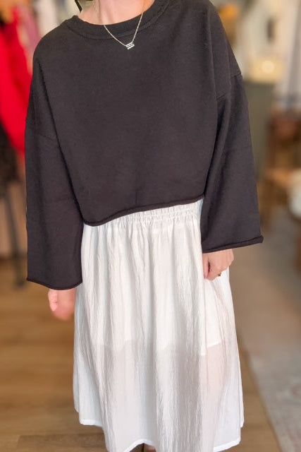 Person wearing a black sweater and white skirt in an indoor setting