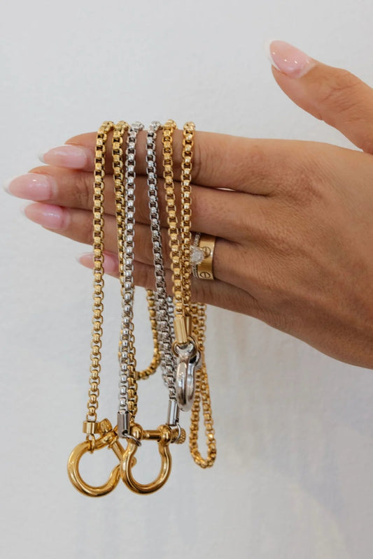 Hand holding three gold and silver chains against a light background