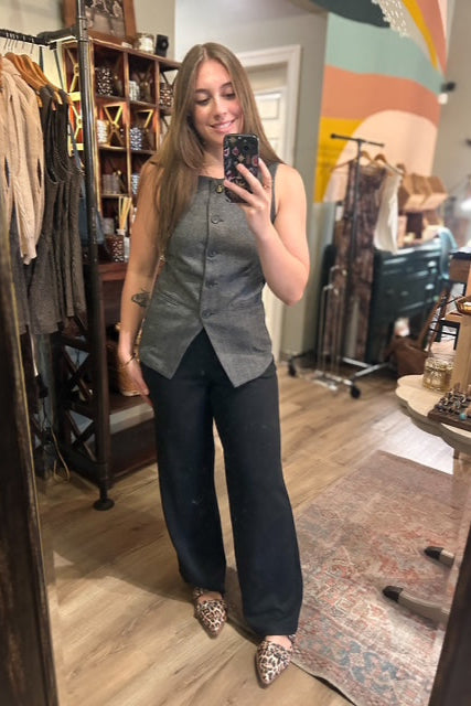 Woman taking a mirror selfie in a clothing store wearing a gray top and black pants.