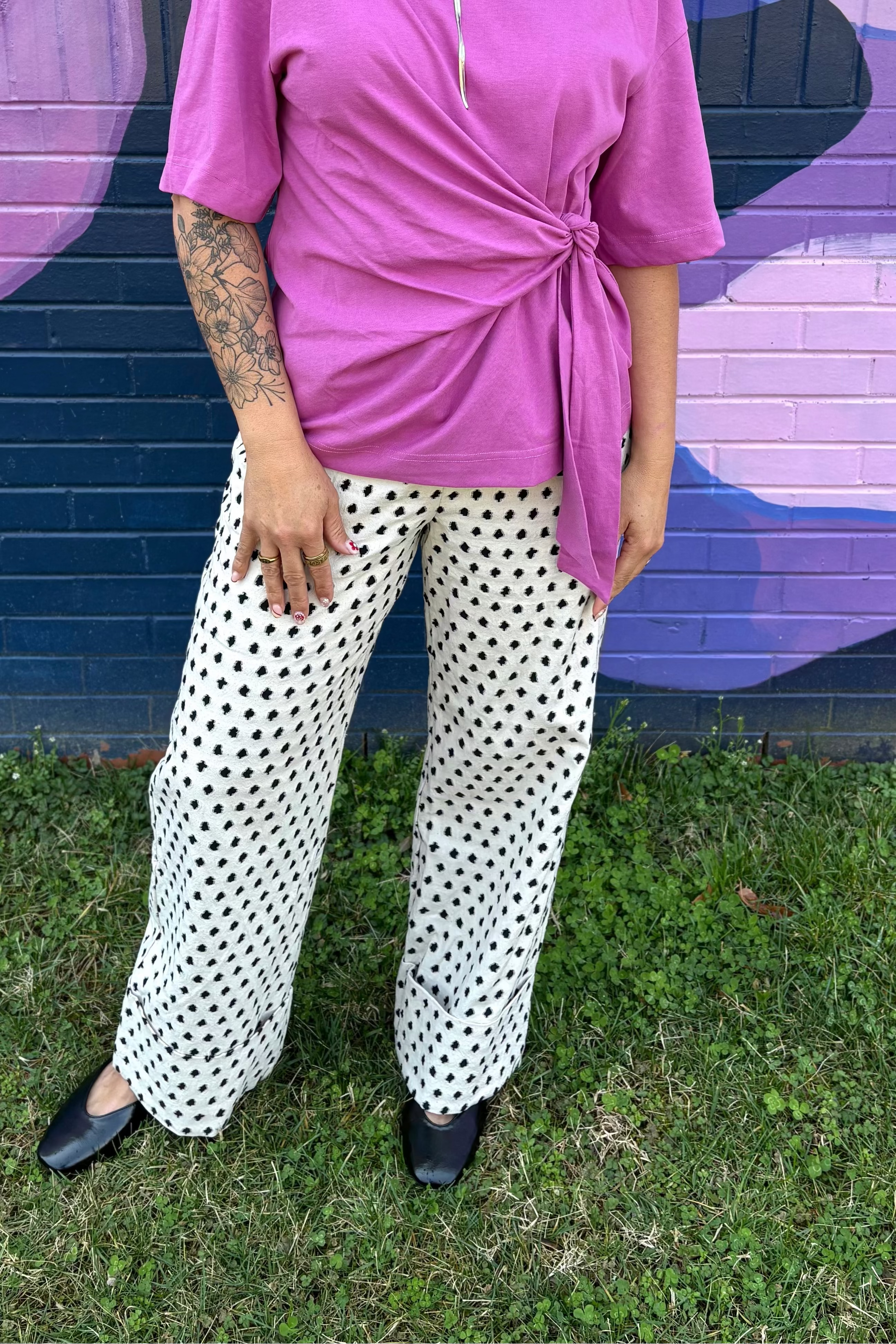 Woman in a pink top and polka dot pants standing in front of a colorful mural.