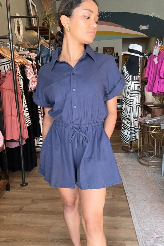 Woman wearing a blue dress standing in a store with racks of clothes in the background.