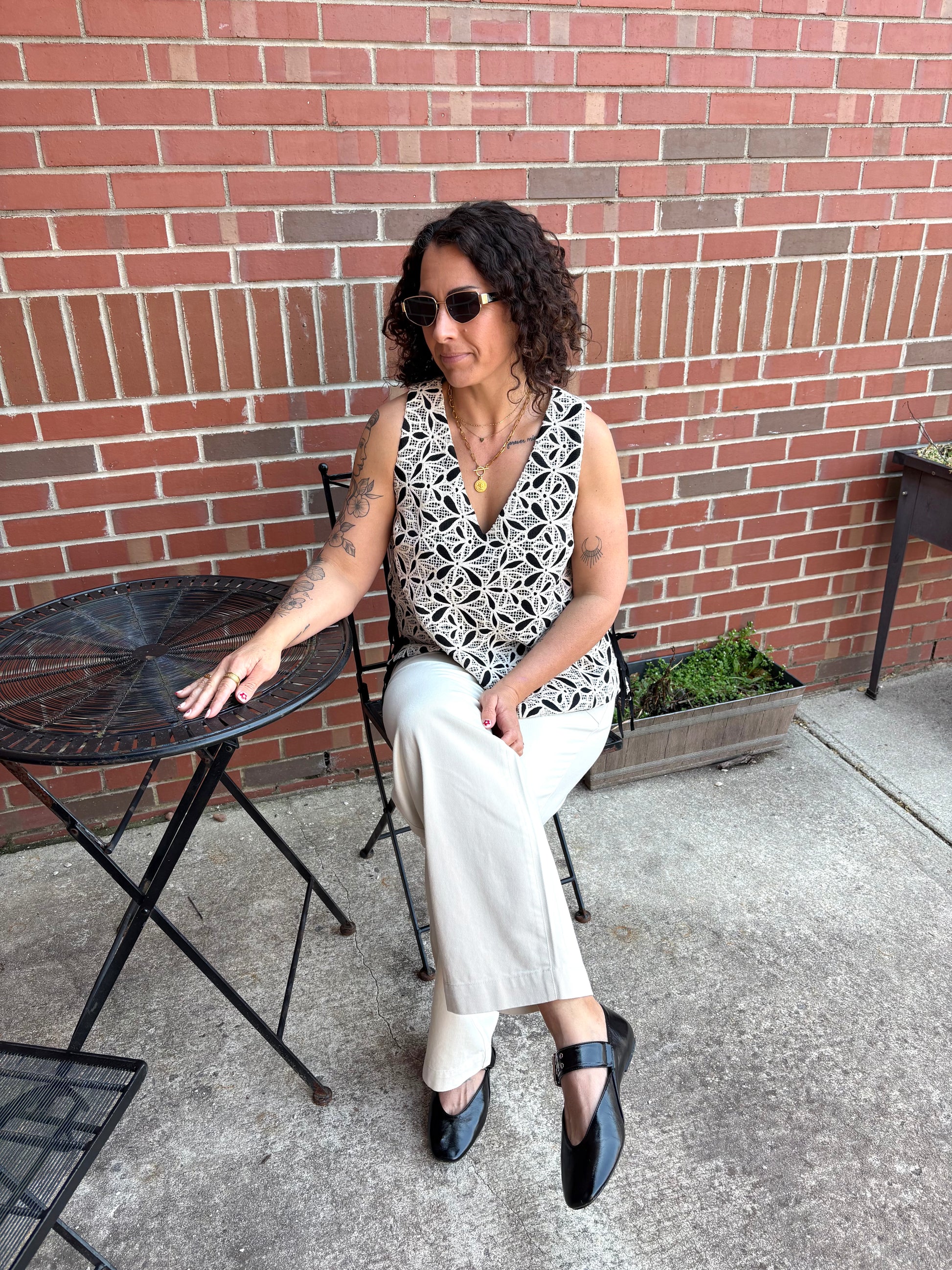 Woman sitting at a small round table outdoors against a brick wall.