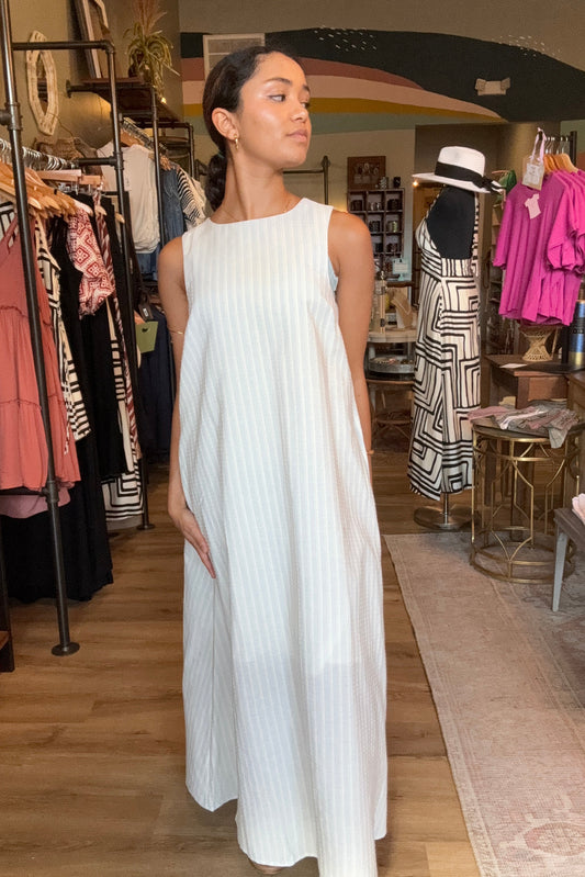 Woman wearing a white dress standing in a store with racks of clothes in the background.