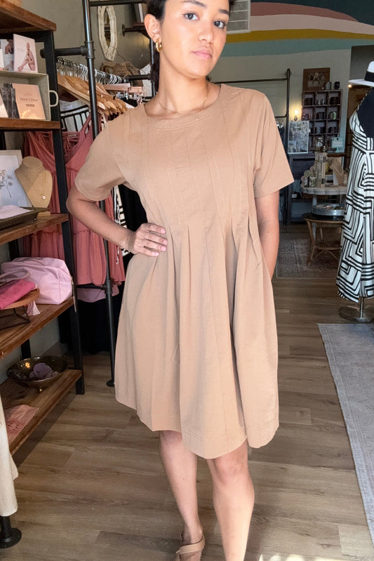 Woman wearing a beige dress standing in a store with shelves and products in the background.