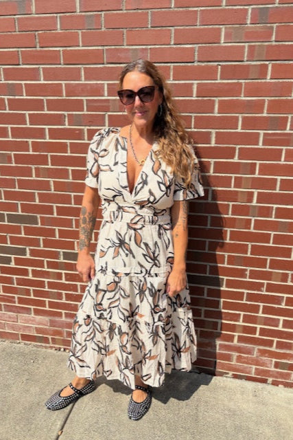 Woman in a floral dress standing against a brick wall
