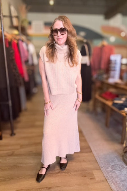 Woman in a light pink sleeveless top and skirt standing in a clothing store.