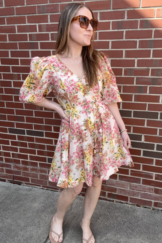 Woman wearing a floral dress standing against a brick wall.