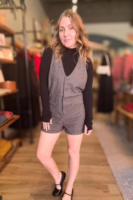 Woman wearing a checkered dress over a black long-sleeve shirt in a store setting.