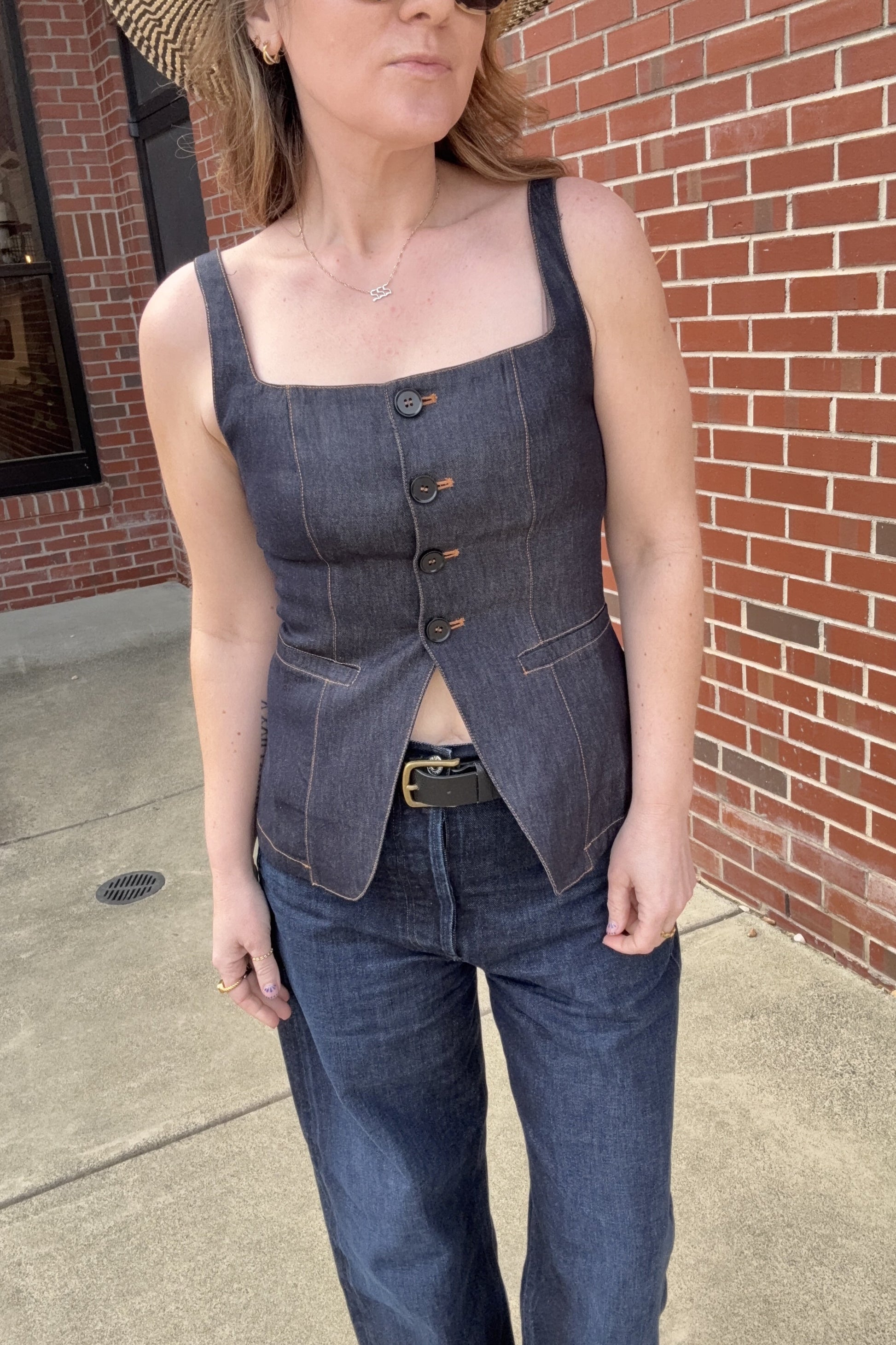Woman wearing a denim outfit standing against a brick wall.