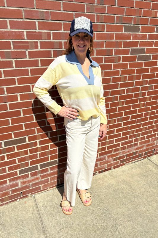 Woman in a yellow top and white pants standing against a brick wall.