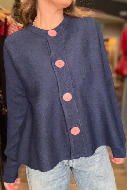 Navy blue jacket with pink buttons worn by a person in a store setting