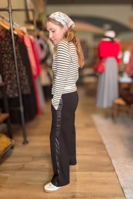 Woman in a striped shirt and black pants standing in a clothing store.