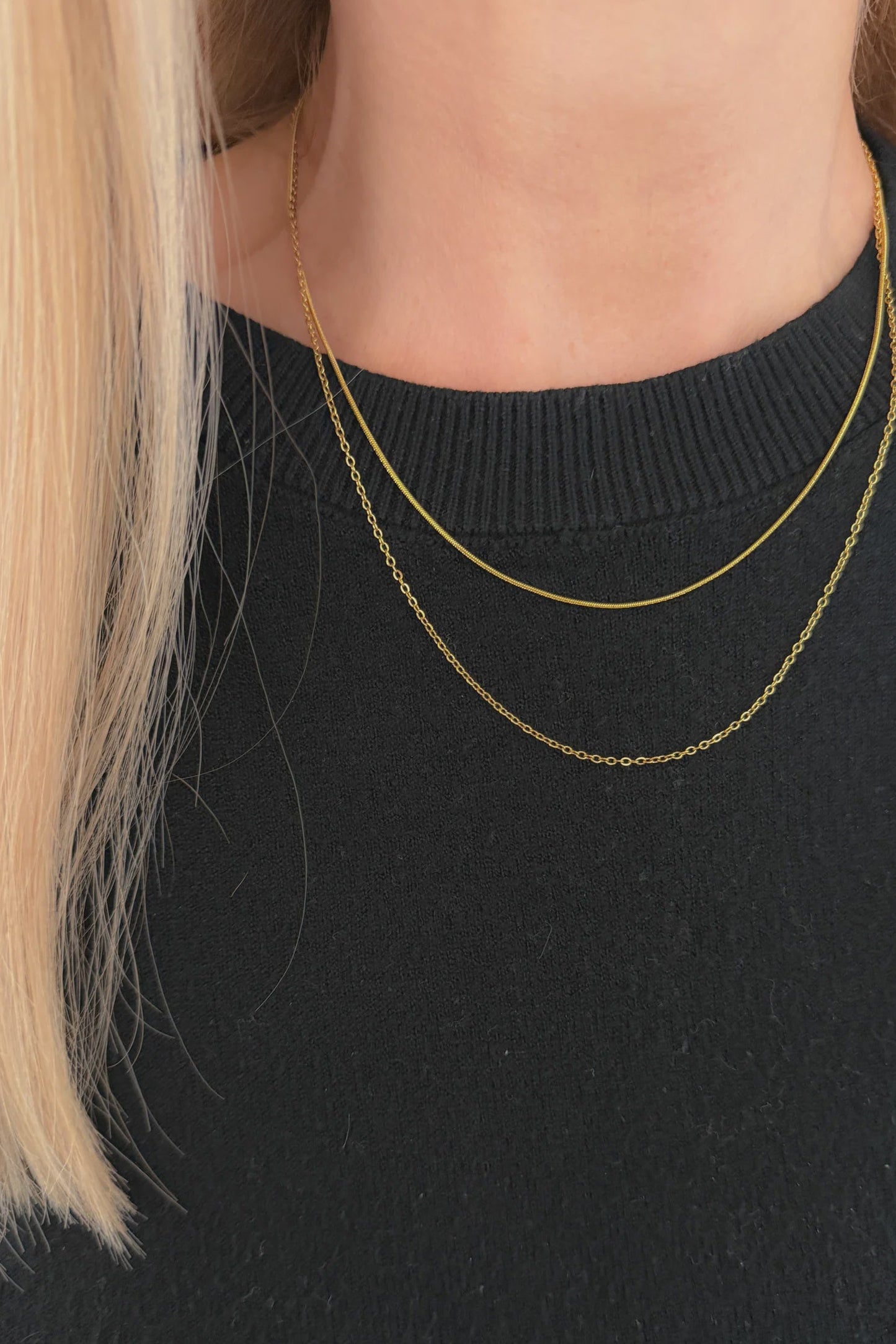 Gold chain necklace worn by a person with blonde hair, against a black background