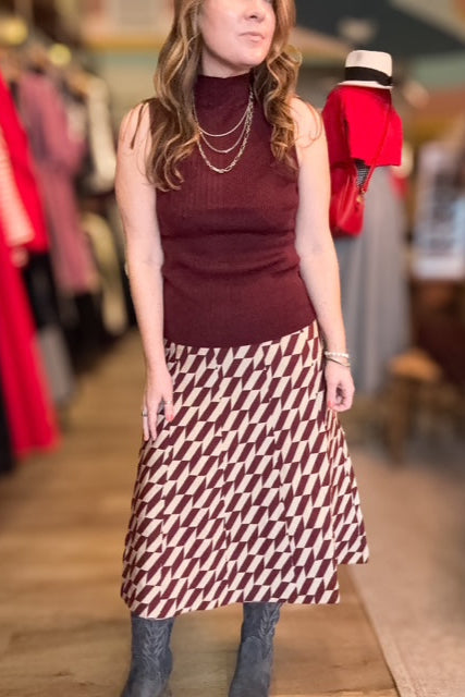 Woman wearing a patterned skirt and sleeveless top in a clothing store.