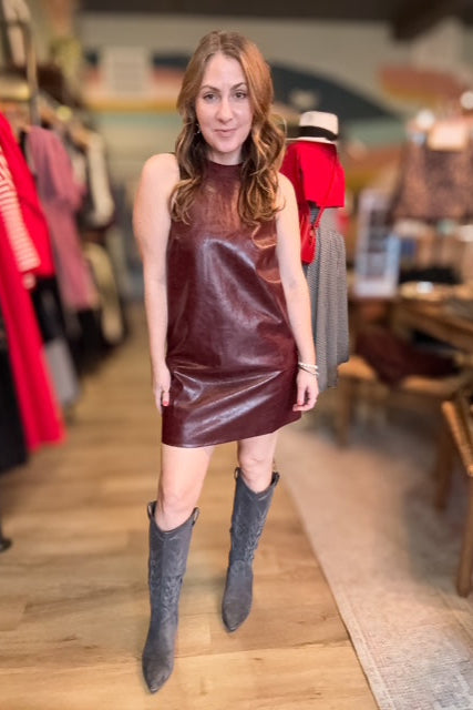 Woman wearing a brown leather dress and gray knee-high boots in a store setting.