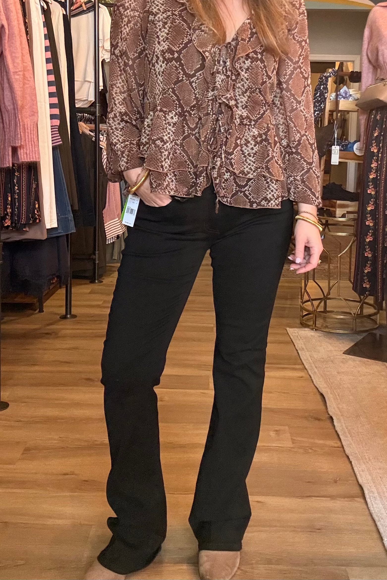 A woman modeling a brown and beige snakeskin print blouse with black flare jeans in a clothing store.
