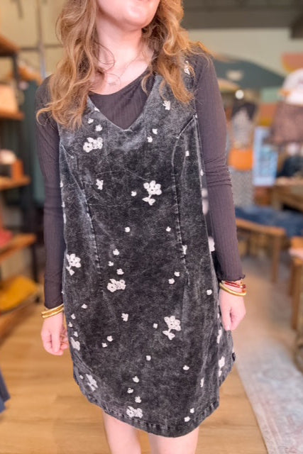 Person wearing a dark gray dress with floral embellishments in a store setting